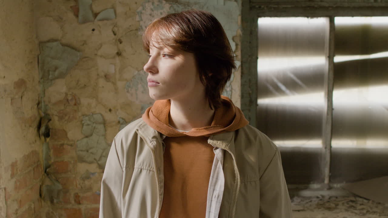 폐허가 된 건물에서 그녀의 머리를 만지는 동안 카메라를 보고 있는 빨간 머리 소녀의 초상화