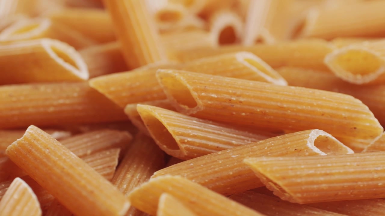 Pasta integrale biologica, maccheroni di semola di grano duro, penne rigate crude in una ciotola di legno. Filmato 4k di alta qualità