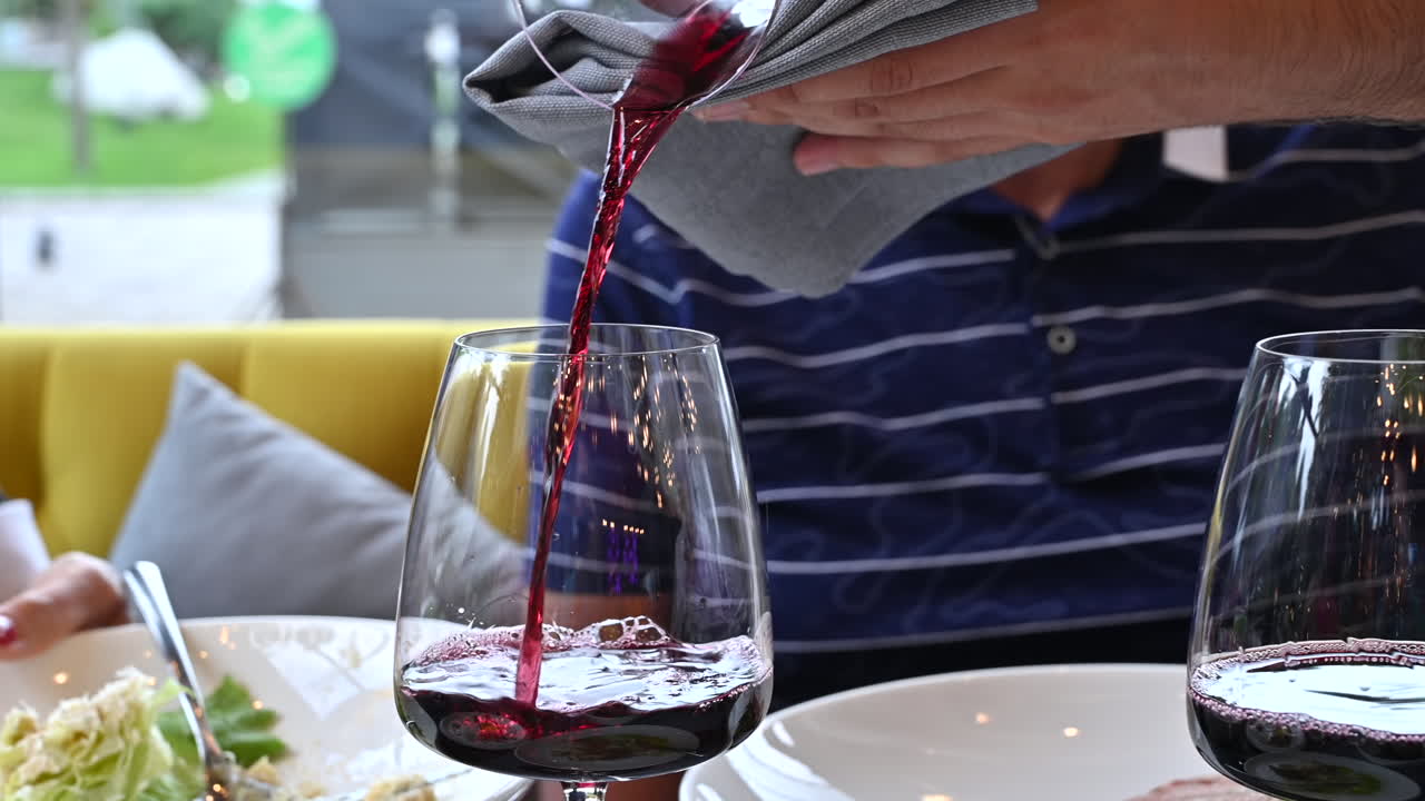 Uomo che versa vino rosso in un bicchiere a un tavolo in un ristorante