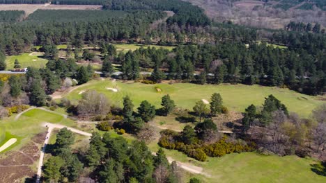 Antena-Giratoria-Sobre-Un-Campo-De-Golf-Que-Revela-Un-Bosque-Verde-Oscuro-Y-Una-Granja-A-Lo-Lejos