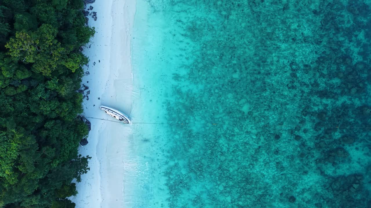 Affascinanti riprese aeree di Monkey Beach sull'isola di Phi Phi, che mostrano acque cristalline color turchese e una barca abbandonata solitaria su una spiaggia sabbiosa incontaminata, senza persone visibili