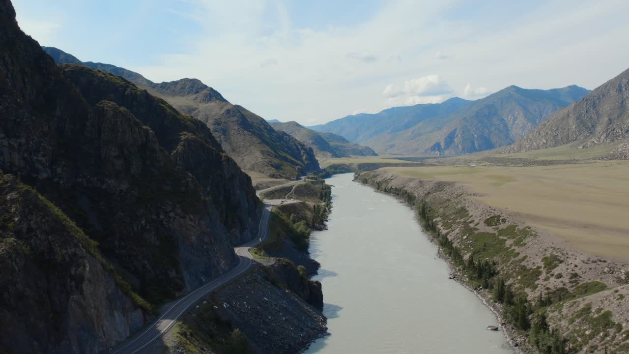 Drone footage of the Chuysky Trakt highway winding along steep rocky slopes and green mountains near the Katun River, Altai Republic, Russia