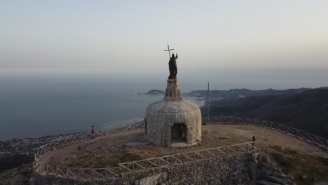 person statue with cross over watching gaeto city, aerial drone fly close view