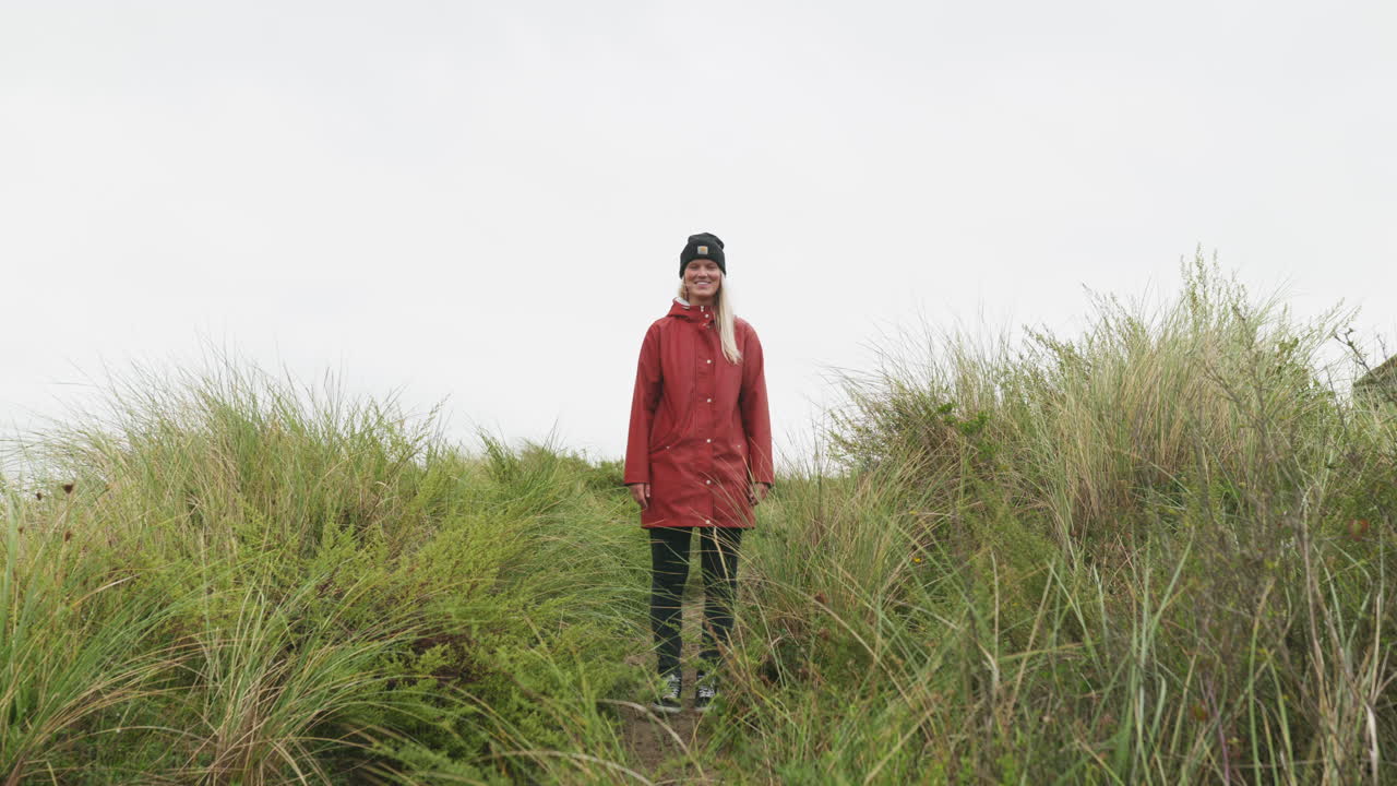 Caucasian Girl In Red Jacket Standing And Walking Away By The Grassy Path Towards The Ijmuiden Beach In The Netherlands
