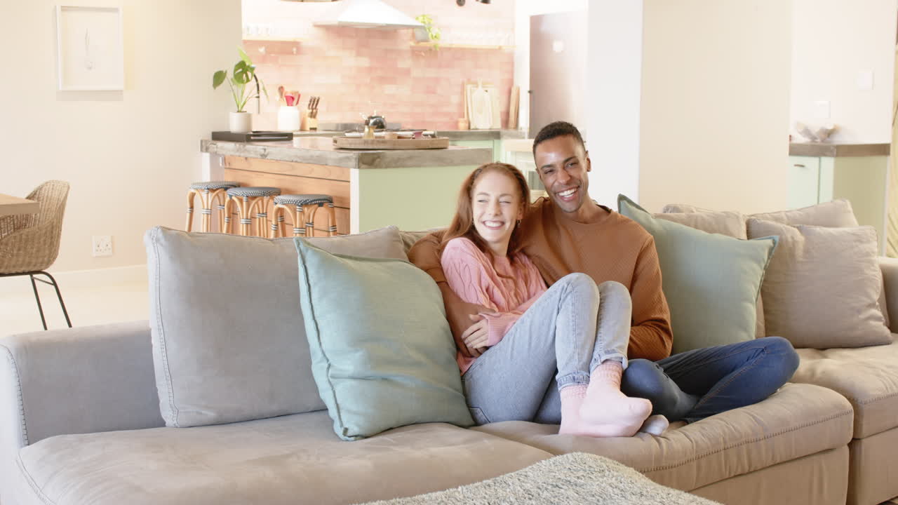 Diverse couple relaxing on cozy sofa at home, enjoying peaceful moment together, copy space