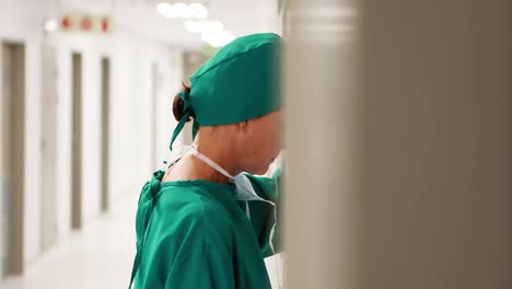 una cirujana tensa apoyándose en la pared en el pasillo.