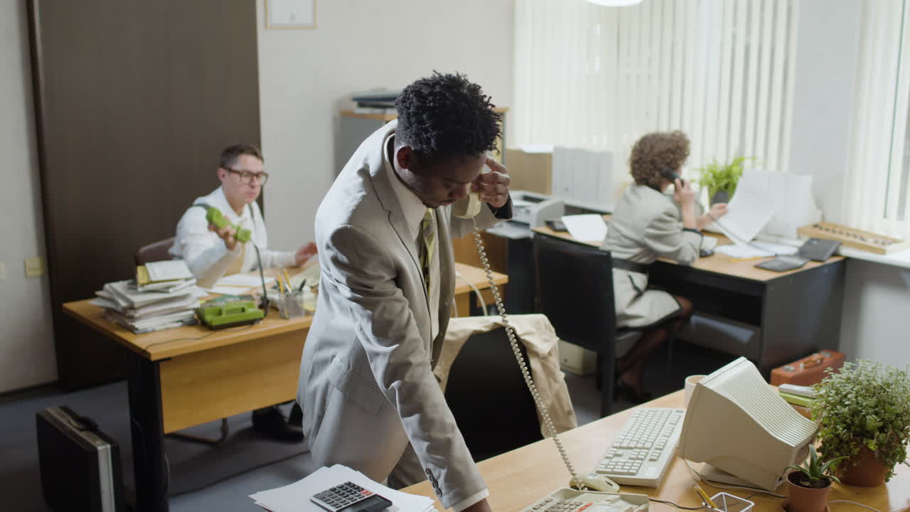 African american businessman working stading near his desk and talking on the phone in a vintage office.