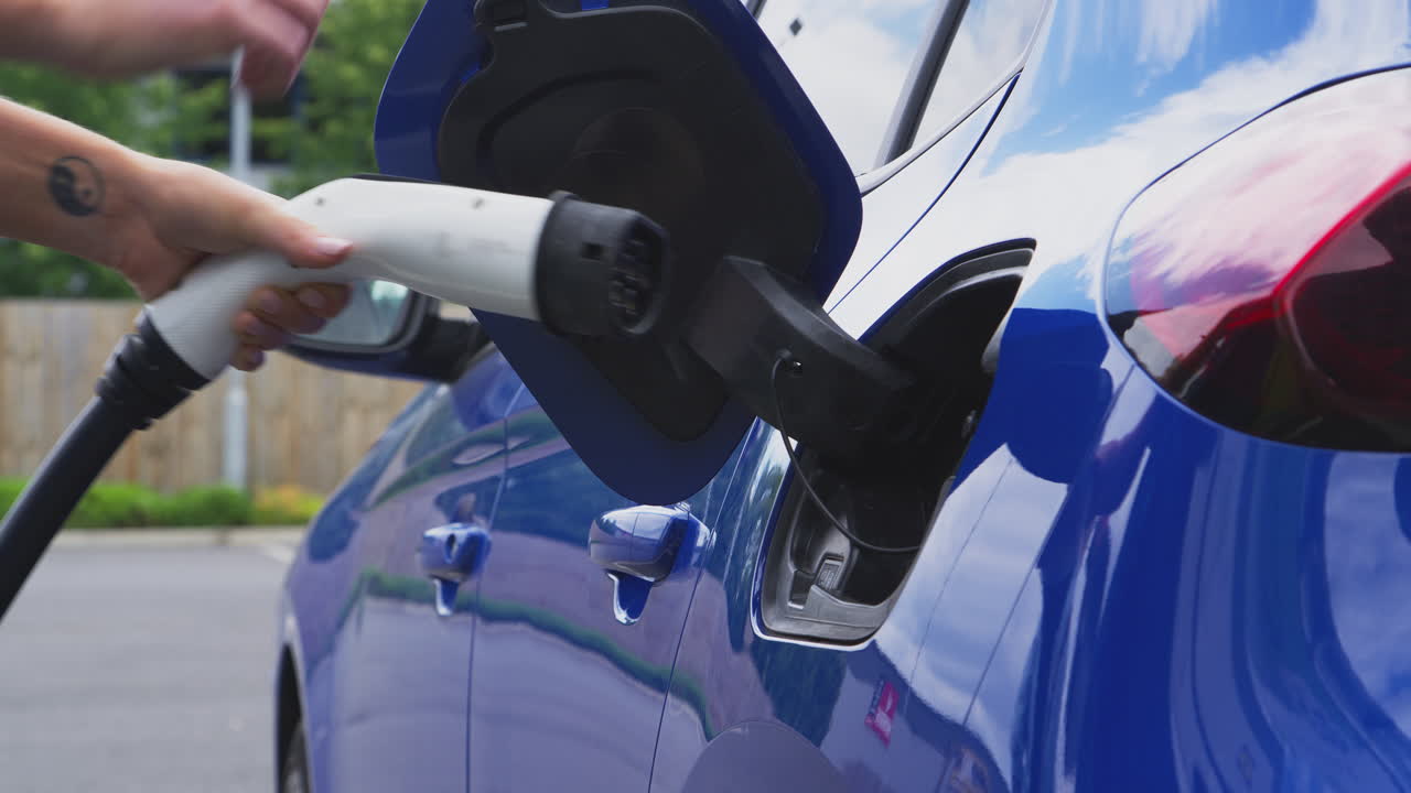 Açık havada çevre dostu sıfır emisyonlu elektrikli arabaya şarj kablosu takan kadın.