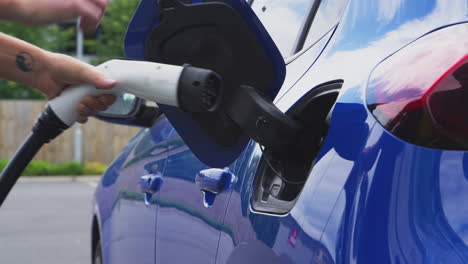 mujer conectando el cable de carga a un coche eléctrico ecológico de cero emisiones al aire libre
