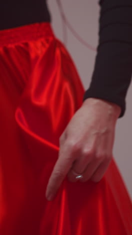 cantante sin rostro en vestido negro y rojo con gracia sosteniendo y girando la vibrante tela roja del vestido en un entorno de estudio. el movimiento dinámico y los colores ricos crean un dramático