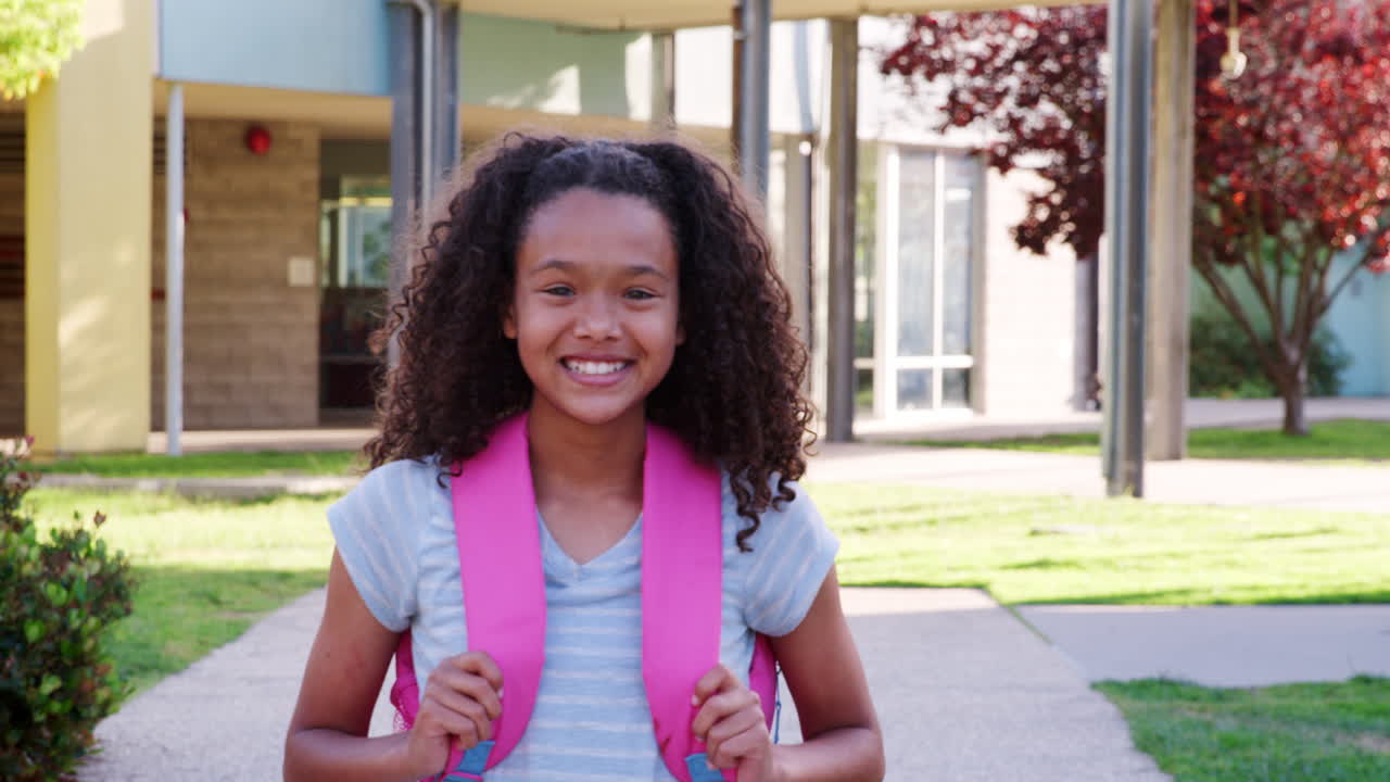 Studentessa che cammina verso la telecamera sorridendo, fuori dalla scuola.
