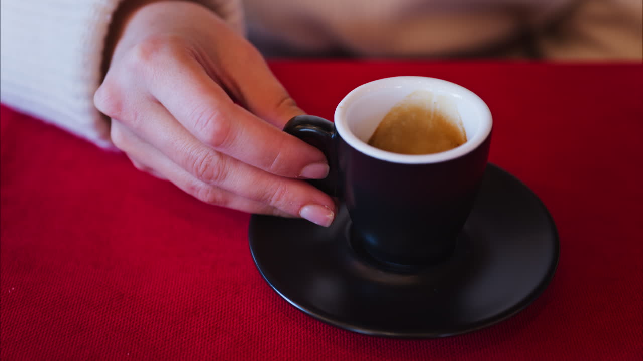 Close up of a woman drinking an espresso out of a black cup on a red tablecloth at a restaurant