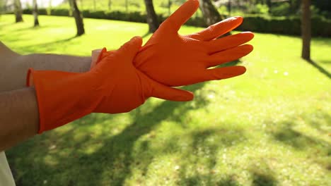 primer plano de las manos del hombre poniéndose guantes de goma naranja