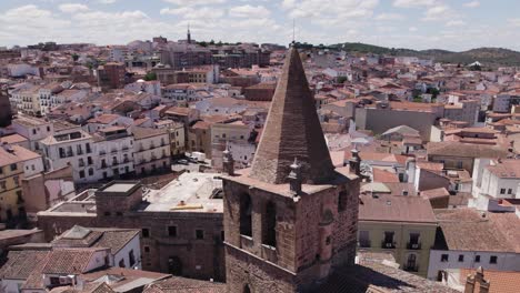 Iglesia-de-Santiago-el-Mayor-aerial-view-circling-catholic-church-tower-spire-in-Cáceres,-Spain