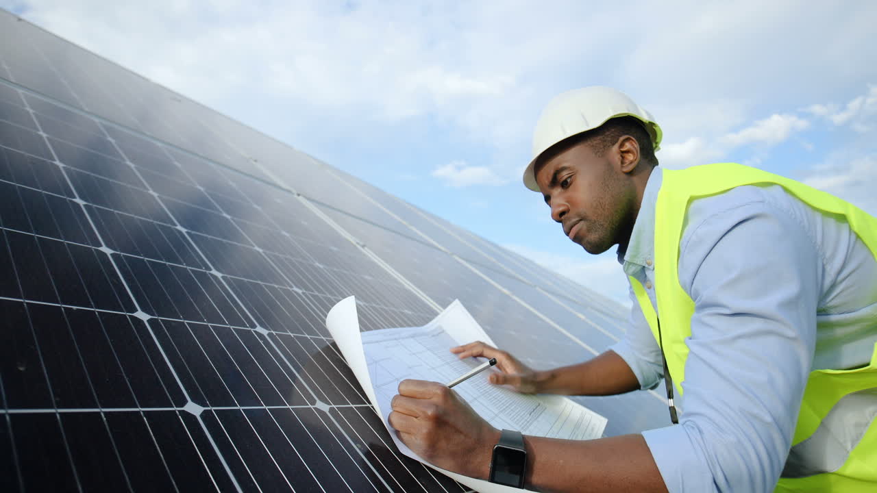 vista lateral de un joven ingeniero afroamericano tomando notas sobre un proyecto en un panel solar