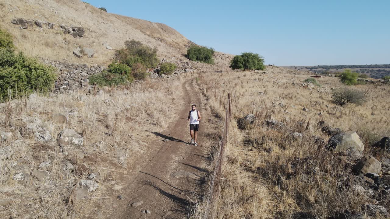 A hiker walking alone along a dirt road in a dry, hilly landscape spending time outdoors in Israel, Golan Heights