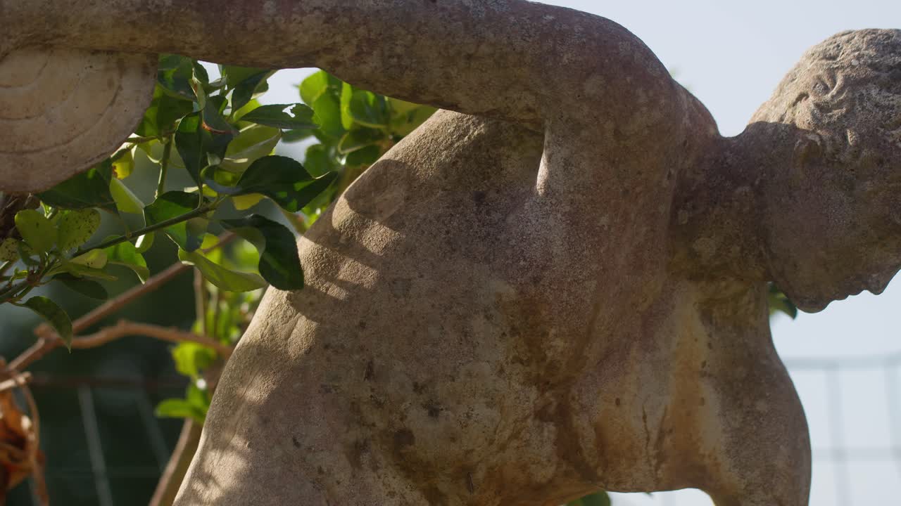 Close-up of an Italian rock statue, green plants casting shadows, and wind blowing, creating a serene atmosphere in Capri