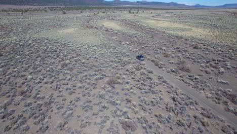 Aerial-above-a-4WD-traveling-on-a-dirt-road-in-the-Mojave-Desert-with-the-Sierra-Nevada-mountains-distant-2