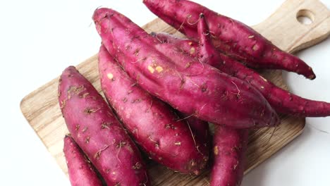 pile of purple sweet potatoes on a wooden cutting board