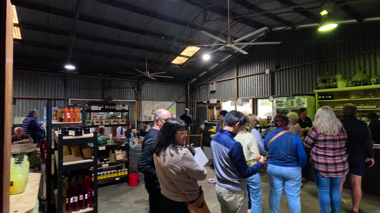 A group of people stand in line inside a rustic farm shop, illuminated by overhead lights, as they wait to purchase local produce in Stanthorpe, Queensland