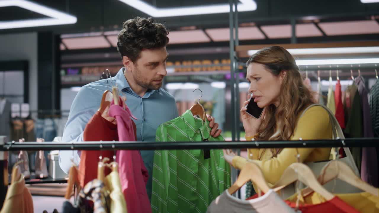 쇼핑 중독자 여성이 가게에서 클로즈업으로 옷을 찾고 있습니다. 고객을 돕는 남자