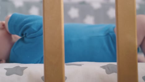 little-child-with-bare-legs-licks-hand-resting-in-modern-cot