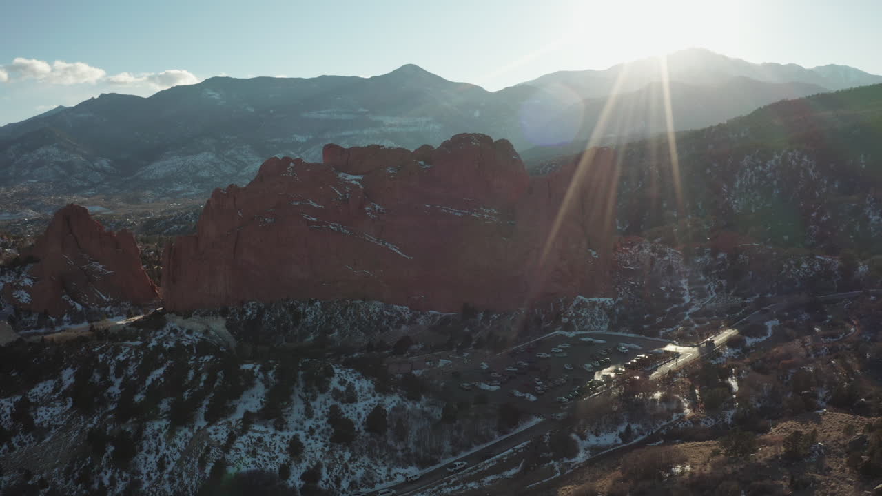 Sunrays illuminate Garden of the Gods. Pikes Peak in background. Aerial parallax.