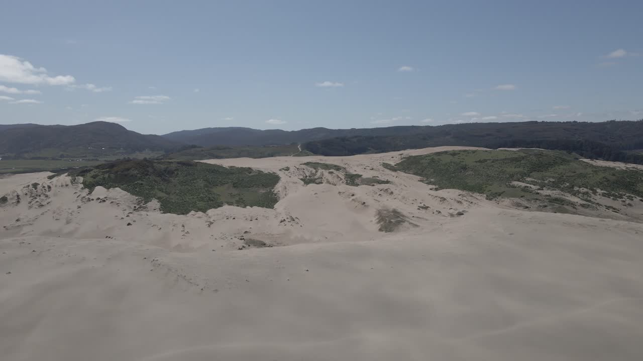 vista aérea de las dunas de arena en llani, chile con parches de verde y las montañas en el fondo
