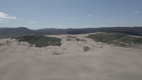 aerial view of the sand dunes in llani, chile with patches of green on it and the mountains in the background