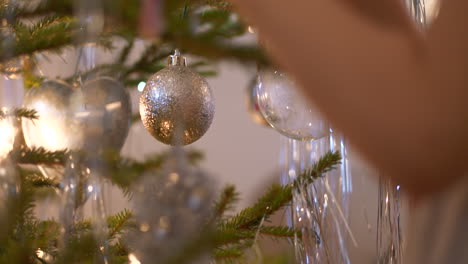 medium shot of young girl's hand decorating real natural christmas tree with x-mas candy