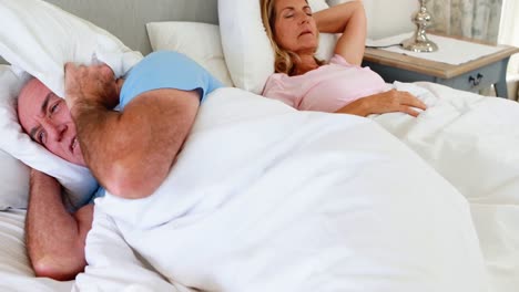 senior man lying on bed and covering his ears with pillow