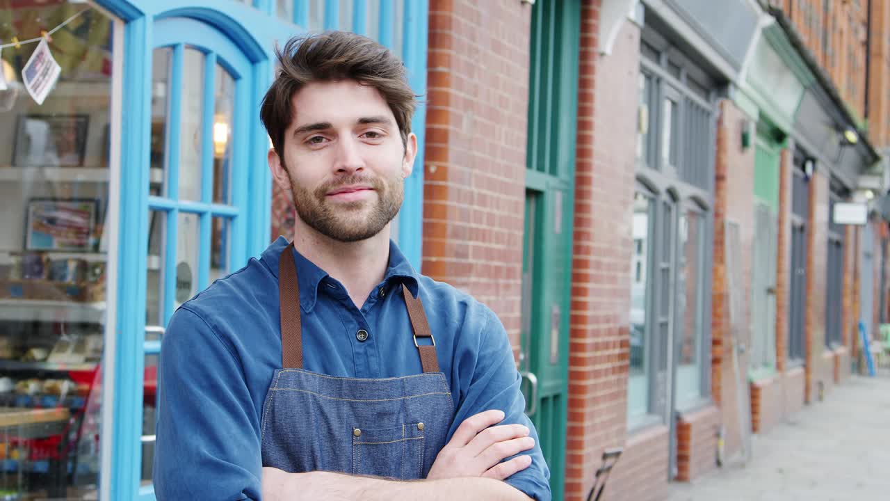 retrato de un hombre sonriente dueño de una pequeña empresa de pie fuera de la tienda en la calle principal local