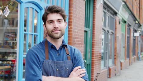 retrato de un hombre sonriente dueño de una pequeña empresa de pie fuera de la tienda en la calle principal local