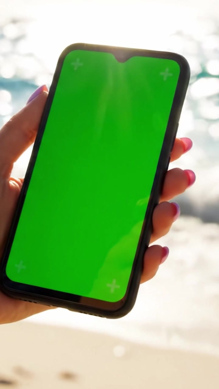 Una Mano Che Tiene uno Smartphone con Green Screen in Spiaggia, Ideale per la Creazione di Contenuti e l'Editing Digitale in un Suggestivo Scenario Costiero
