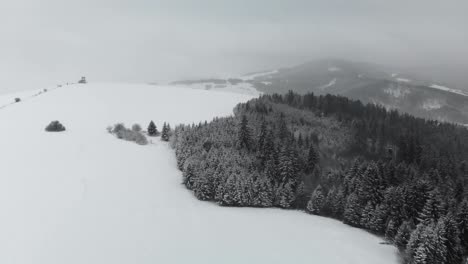 Aerial-forward-over-snow-covered-landscape-with-hills-and-snowstorm-in-background