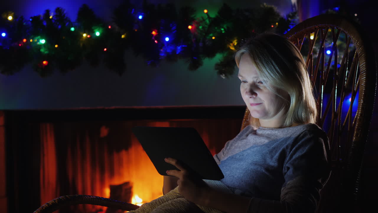 mujer usa una tableta contra el fondo de una chimenea y guirnaldas festivas