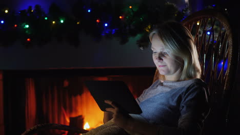 mujer usa una tableta contra el fondo de una chimenea y guirnaldas festivas