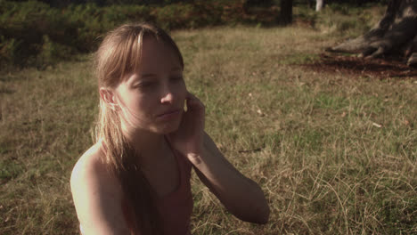 cose up of a young woman sitting in the park's grass with the sun shining on the back of her head