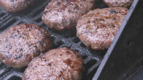 group of beef burgers gently cooking on hot iron grill on bbq cooked outside in natural lighting. delicious juicy meat grilled.