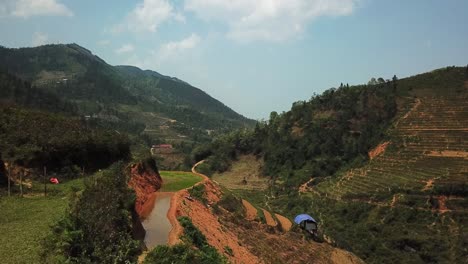 a girl runs to the edge of a hill and puts her hands up for help or attention, looking towards a blue shelter