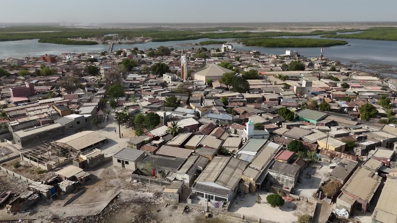 Drone approach Joal Fadiouth shell island village in Senegal, showing houses, boats and coastal community around the famous cemetery
