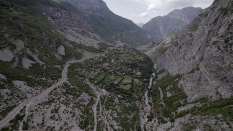 Video-De-Drones-De-Un-Avión-Que-Avanza-A-Vista-De-Pájaro-En-La-Autopista-Sh20-En-Albania,-A-La-Altura-De-Javor-Y-Mreg-Con-Ambas-Ciudades-En-La-Escena,-Se-Pueden-Ver-Pequeñas-Casas-De-La-Ciudad,-Cielo-Nublado