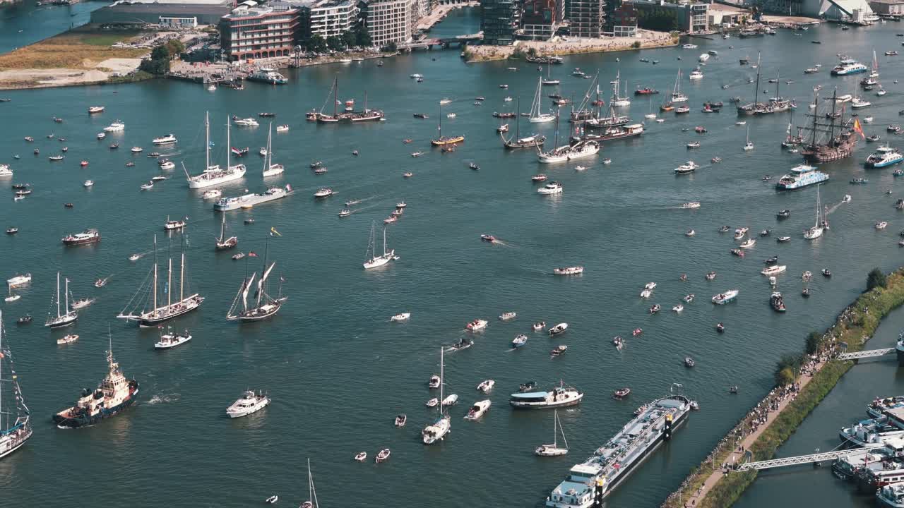 Aerial orbit establishing over clustered sailboats during Amsterdam busy sailing celebration in waterway