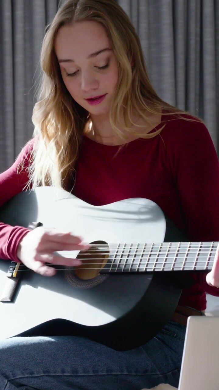 Vertical video: Playing woman in red top, jeans after placing guitar practicing with laptop at home