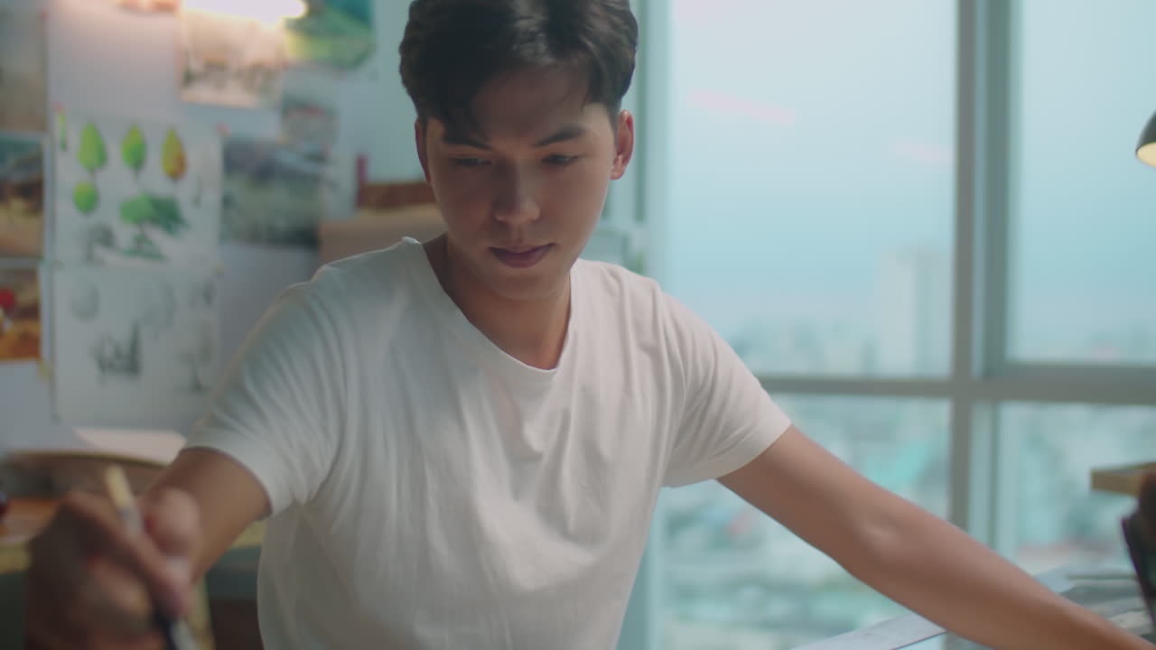 Asian Painter Drawing Picture at Desk in Studio
