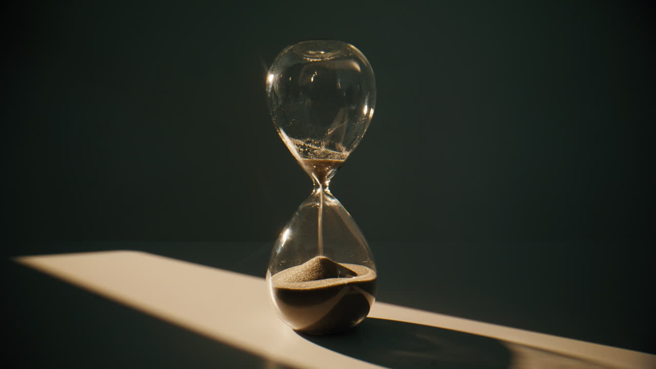 Closeup sand falling hourglass standing at table in evening room. Gold grains