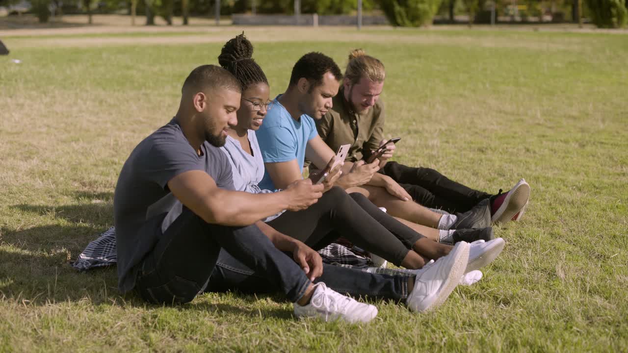 jóvenes alegres sentados en fila y usando teléfonos inteligentes.