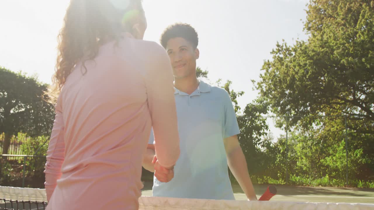 video de una feliz pareja biracial jugando al tenis en la cancha