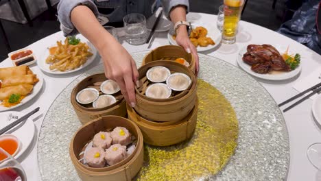 hands arrange bamboo steamers filled with dim sum on a table. bright lighting highlights the vibrant spread of dishes