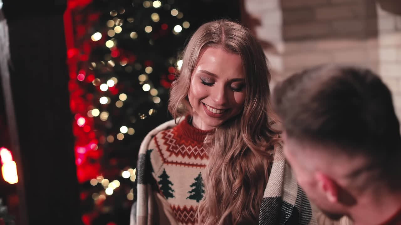 Smiling woman in knitted Christmas sweater. Beautiful young woman talking to a boyfriend and smiles on Christmas tree background.